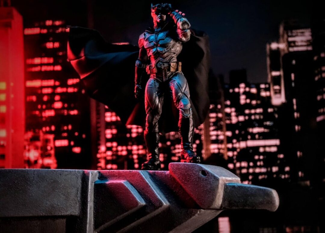 Batman: Noel action figure perched on a rooftop ledge, overlooking a detailed cityscape, showcasing dynamic posing and McFarlane Toys' intricate sculpt and design